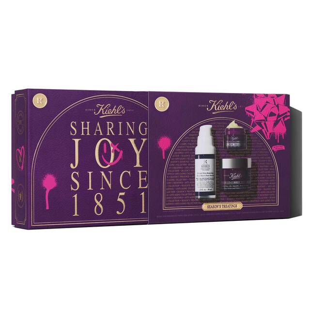 A graphic featuring a rectangular purple and pink Kiehl's "SEASON'S TREATINGS ANTI-AGING COLLECTION" gift set box being open, which contains a white and purple bottle of Retinol Skin-Renewing Daily Micro-Dose Serum, a small purple jar of Super Multi-Corrective Eye Zone Treatment, and a larger purple jar of Super Multi-Corrective Cream.